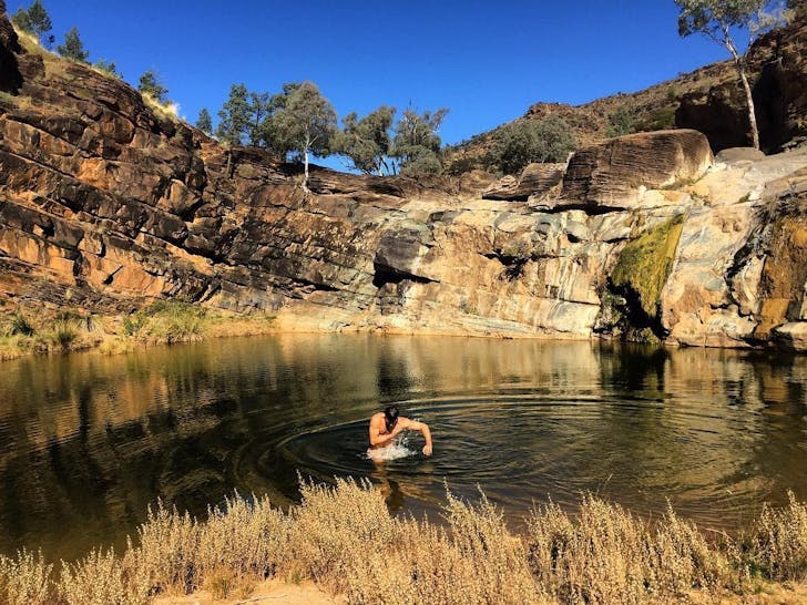 A person swims in a flat natural pool fringed by rock face