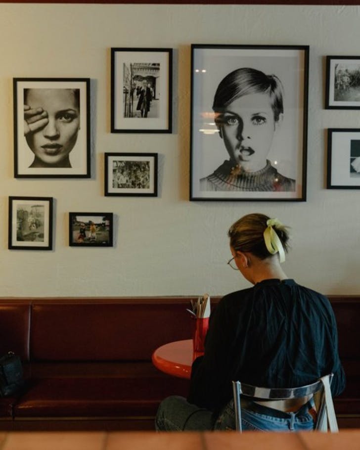 A person sits at a table facing a display of chic wall art at Blondie Diner. 