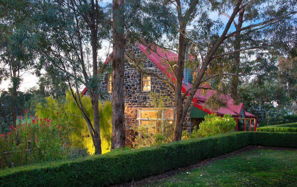 A bluestone house lit up at dusk surrounded by trees, one of the best accomodation Daylesford options.