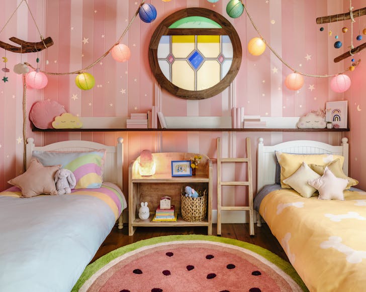 A pastel bedroom with two small beds and colourful lanterns.