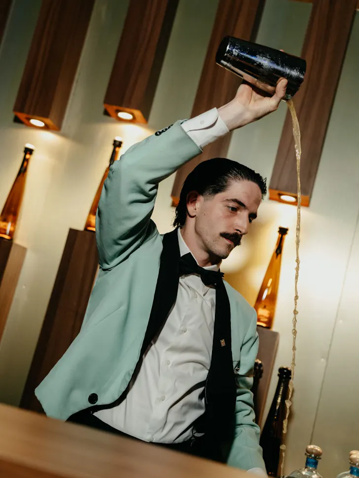 A waiter in a duck-egg blue suit pours a cocktail in Boadas CocteleriÌa.