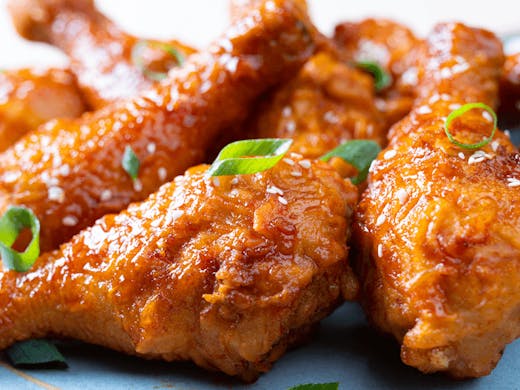 A group of sticky fried chicken drumsticks on a plate.