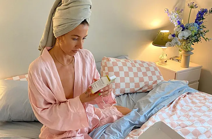 A women in a robe sitting on her bed looking at skincare options