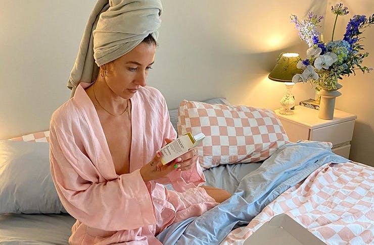 A women in a robe sitting on her bed looking at skincare options
