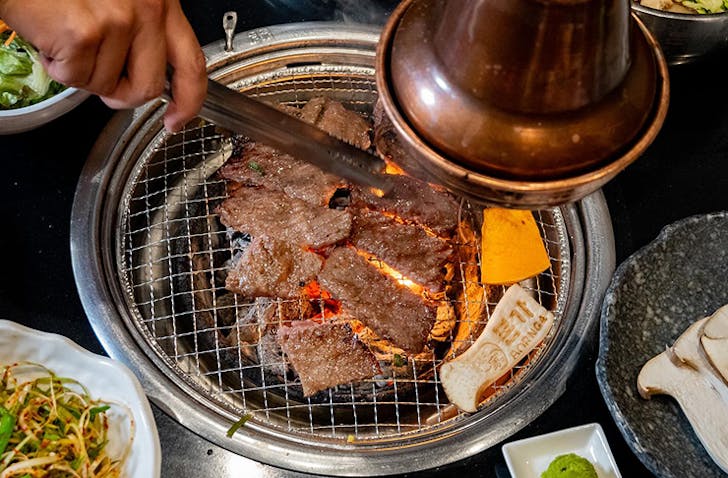 A person using silver tongs to turn over semi-cooked meat on a Korean BBQ at one of the best Korean BBQ restaurants in Melbourne called Bornga