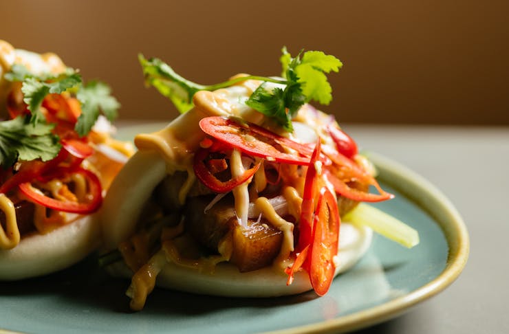 Two bao buns sit on a blue plate. They are filled with pork and coriander slaw.