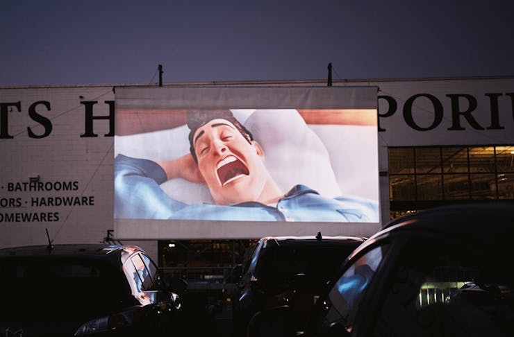 An outdoor cinema screen with a cartoon movie playing. 