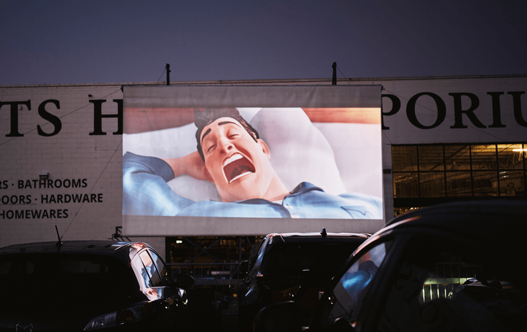 An outdoor cinema screen with a cartoon movie playing. 