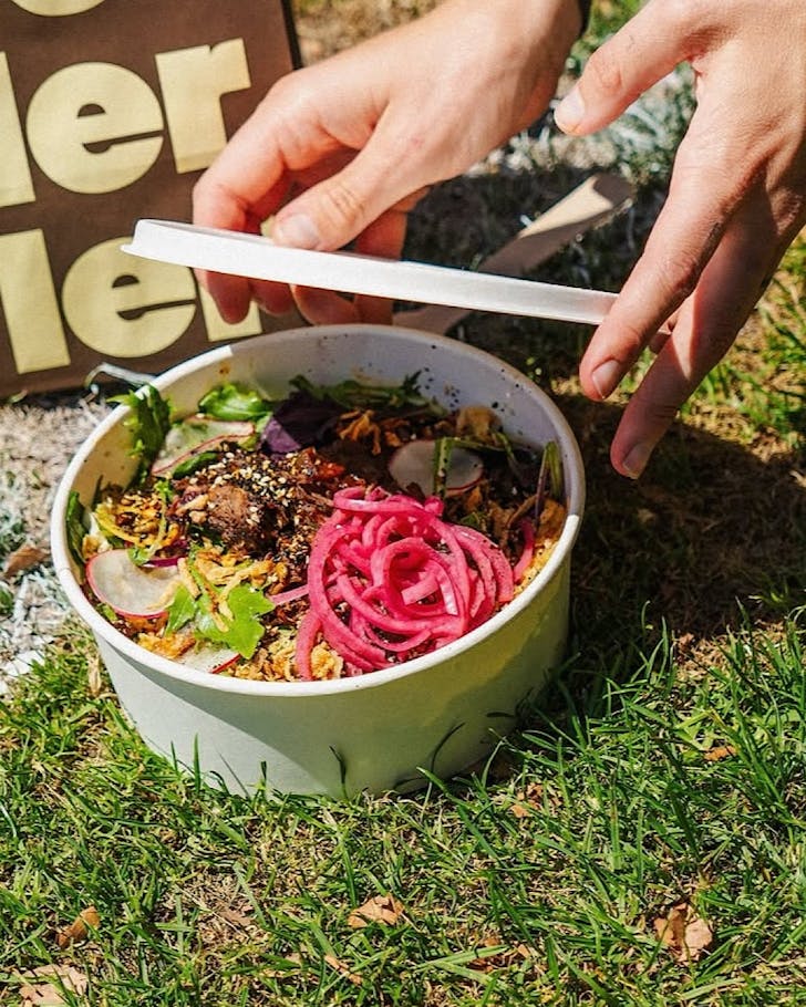 Somebody puts a lid on a salad bowl that's on the grass beside a berry smoothie.