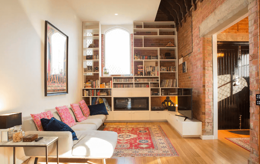 Brick walls, warm coloured furnishings and a glass table in one of the best airbnbs in Melbourne.