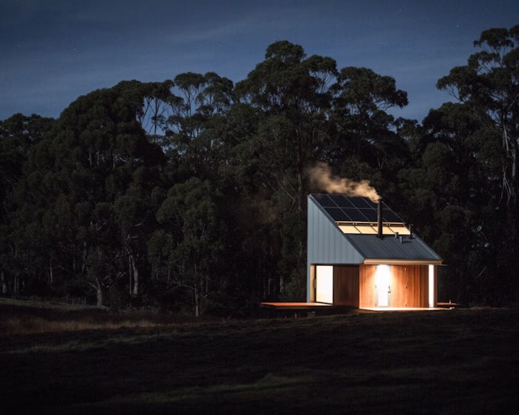 A view of Bruny Island Hideaway Australia tiny house at night with lights on and smoke coming from the chimney