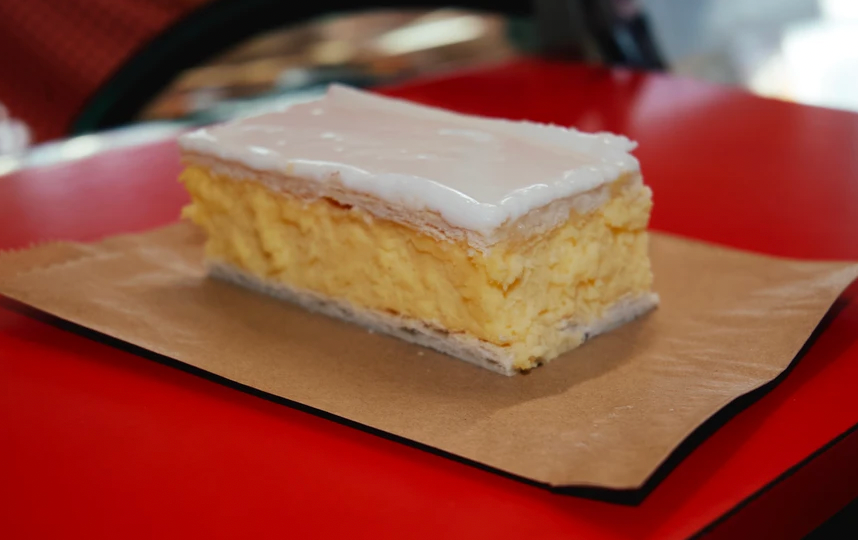 A vanilla slice with thick icing on a red table, a best vanilla slice victoria contender.