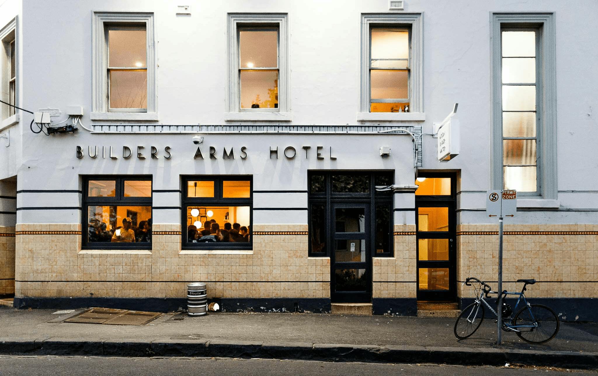 The exterior of a pub with the lights on and people inside. 