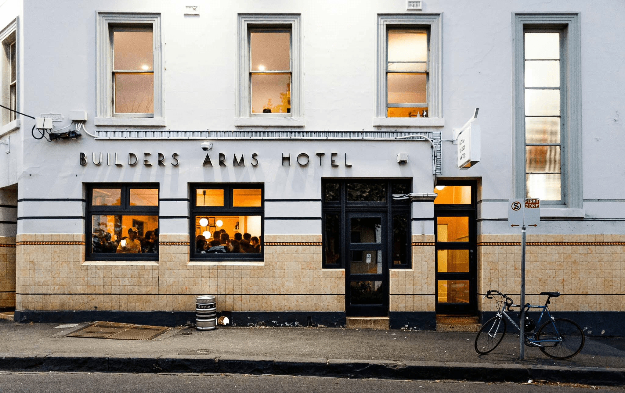 The exterior of a pub with the lights on and people inside. 