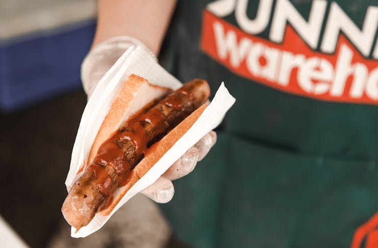 A bunnings staff member holding up a sausage in a slice of white bread.