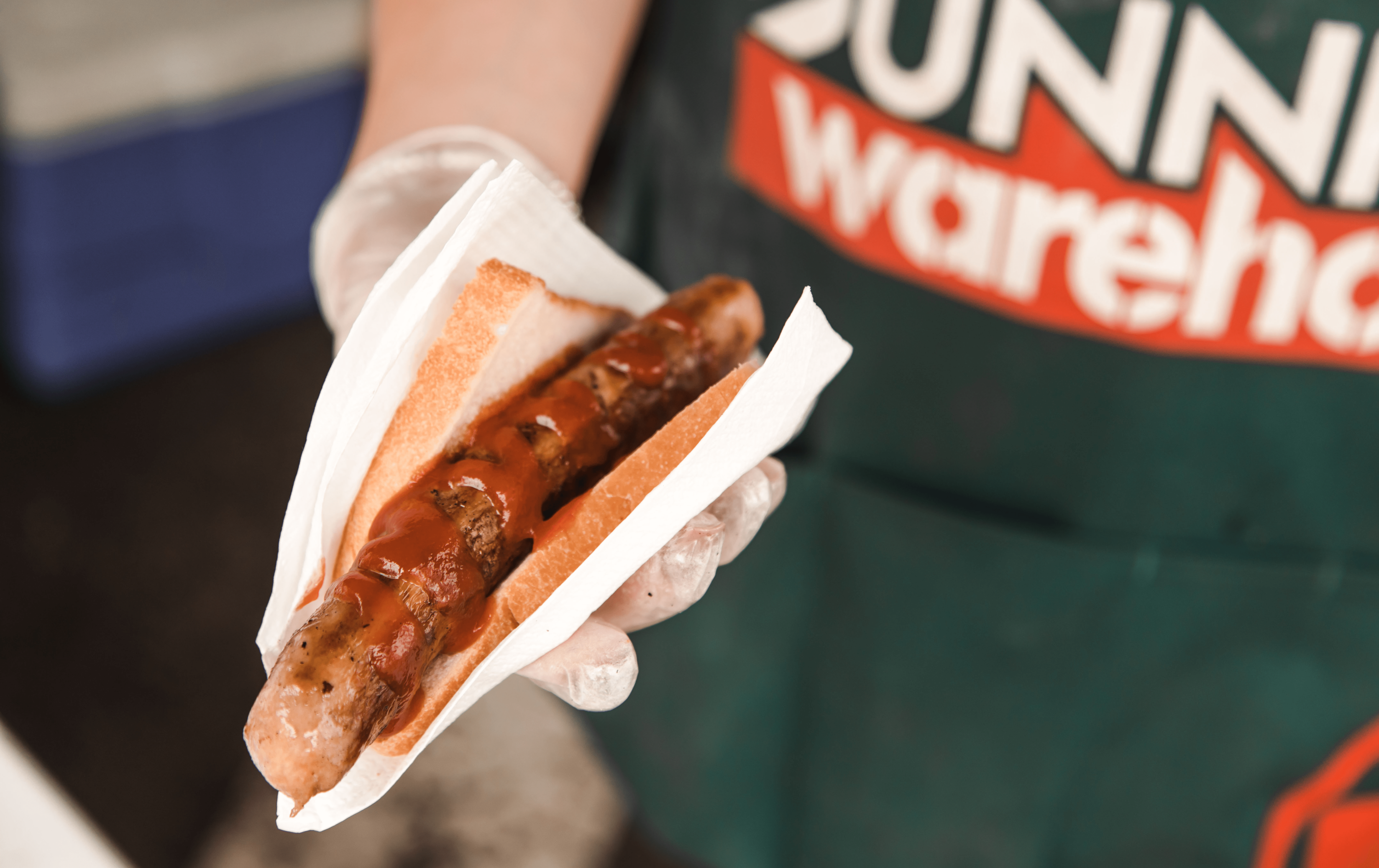 A bunnings staff member holding up a sausage in a slice of white bread.