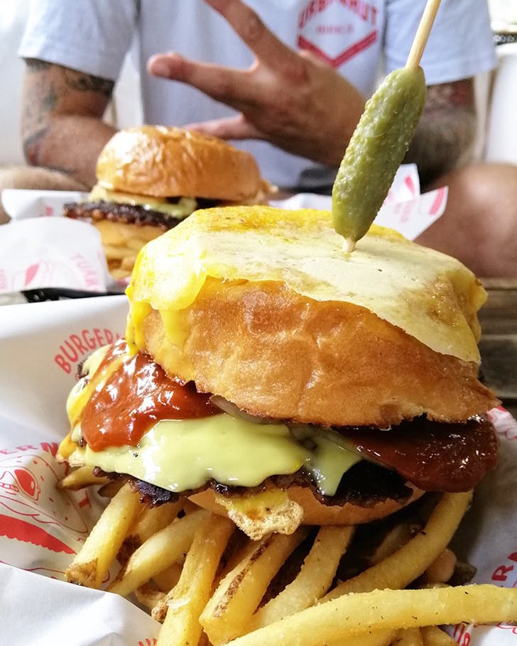 Someone poses by two stacked burgers at Burgernaut.