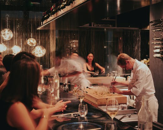 A busy kitchen with a motion shot of two chefs preparing omakase for a bar of guests