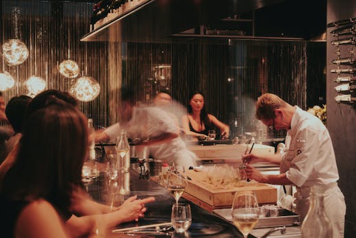A busy kitchen with a motion shot of two chefs preparing omakase for a bar of guests