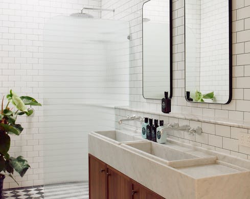 A spa-style bathroom with white countertops, large mirrors and a rainfall shower