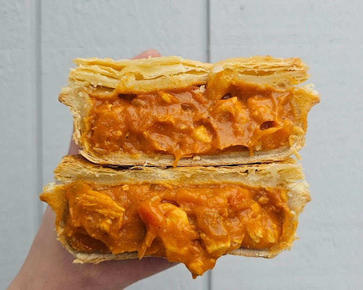 Cross-section of a flaky pastry pie stuffed to the brim with butter chicken. 