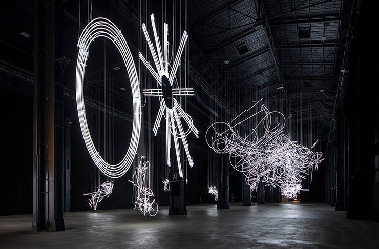 Several large-scale neon light installations in a dark warehouse.