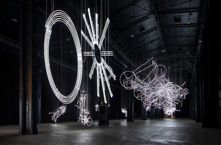 Several large-scale neon light installations in a dark warehouse.