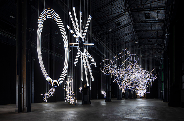 Several large-scale neon light installations in a dark warehouse.