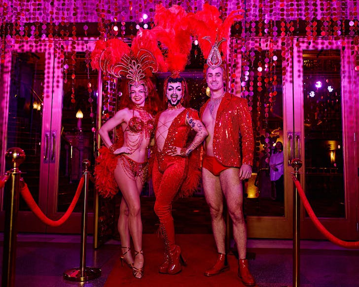 Hugo Grrrl poses with two others in saucy red outfits with the perfect amount of feathers.
