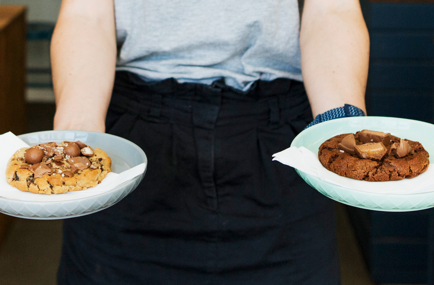 A waitress holds a plate in each hand with a housemade cookie on each.