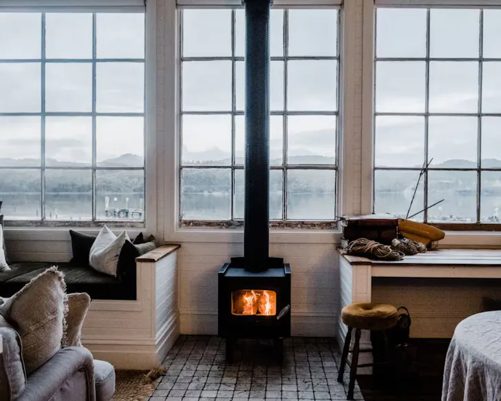 An infoor fire burns by a window looking out to the water at Captain's Rest lake house Airbnb Tasmania