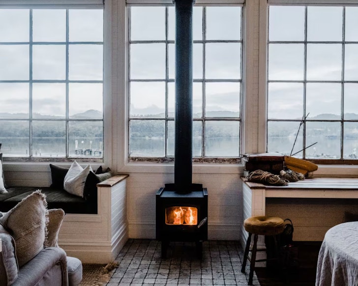 An infoor fire burns by a window looking out to the water at Captain's Rest lake house Airbnb Tasmania