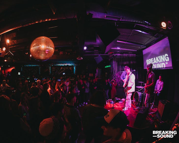 A band is lit in pink light and plays to a crowd at Cassette 9, packed in under a giant disco ball.