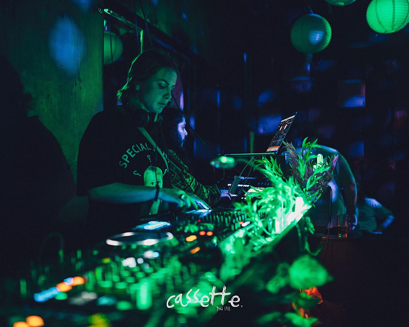 A woman DJs at Cassette Nine, lit in green light. 