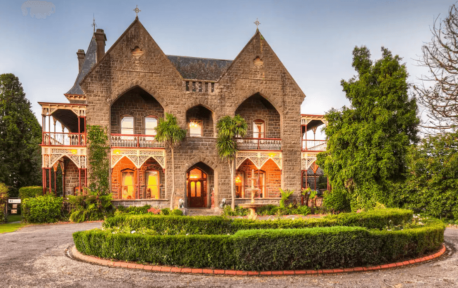A large castle style building with a garden in the front of the shot.