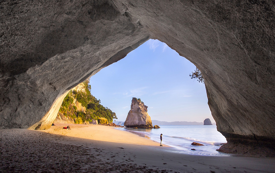 The Cathedral Arch at Cathedral Cove with a person silhouetted in the distance.