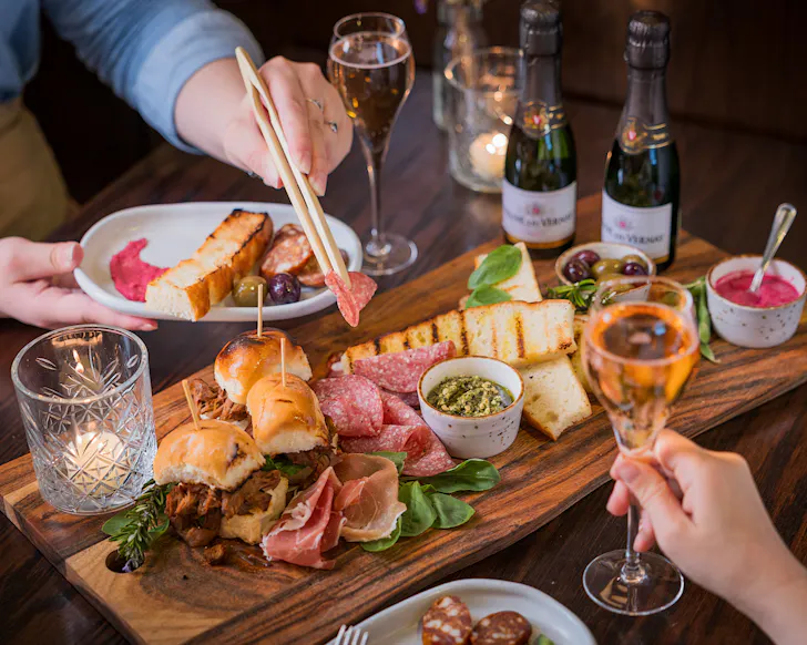 Two people tuck into a platter of charcuterie and sliders at Caucus.