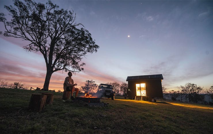 dusk shot of the tiny house, with a person by a campfire outfront