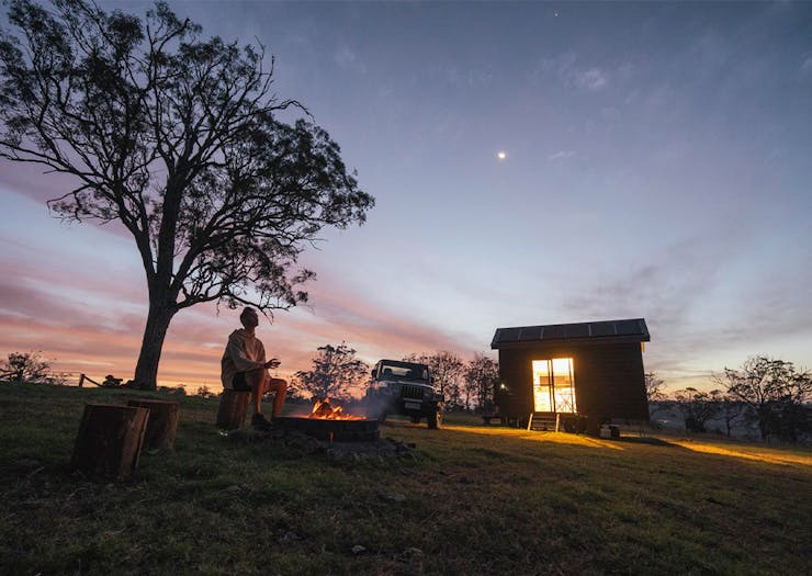 dusk shot of the tiny house, with a person by a campfire outfront