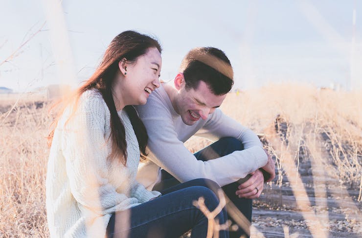 Two people laugh while sitting on a hill together.