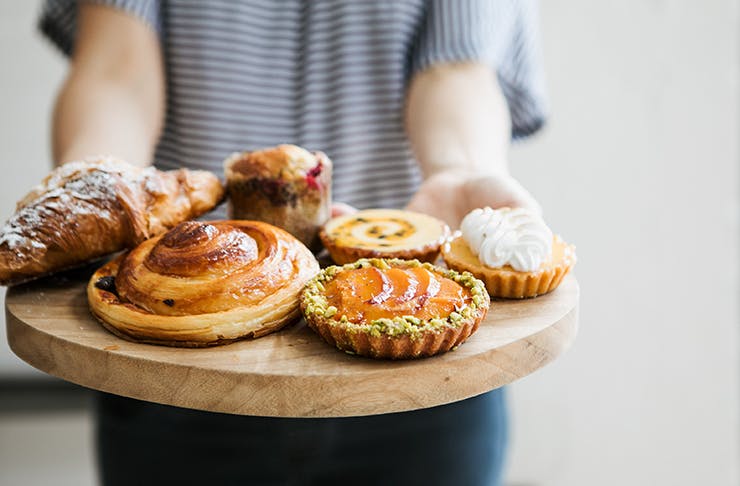 A timber board filled with danishes, tarts and croissants.