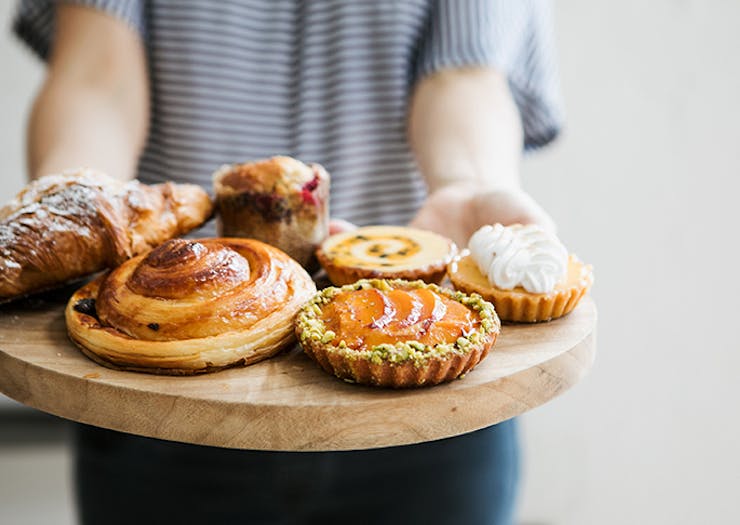 A timber board filled with danishes, tarts and croissants.