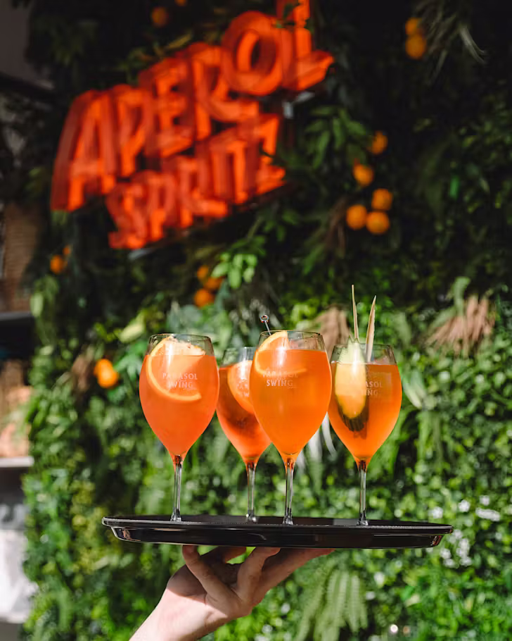 A bartender holds a tray of Aperol spritz.