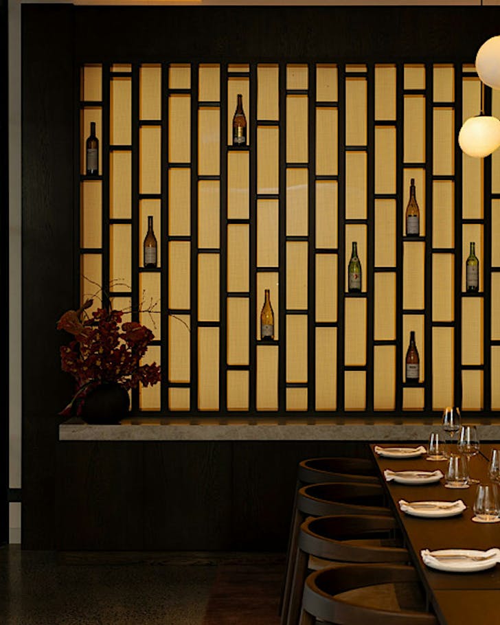 A backlit wall of wineglasses in the background of a swish table setting.