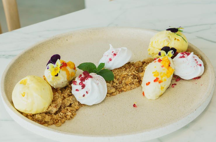 Plat of deconstructed pavlova with biscuit crumbs and ice cream on a white marble table.