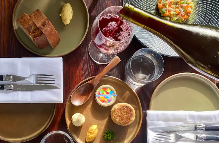 A plate of food and bread on a table and red wine pouring into a glass at Jano Bistro