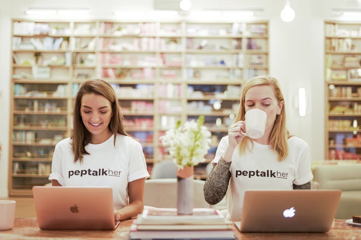 two young women sit a desk with a laptop