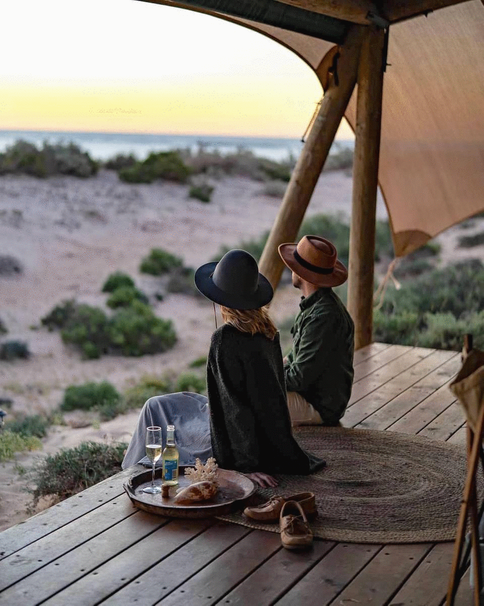 A couple sit on a glamping eco tent at sunset. 