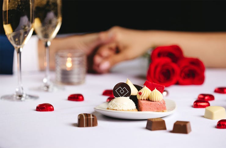 Two people hold hands over a valentine's day petit fours at the Cordis.