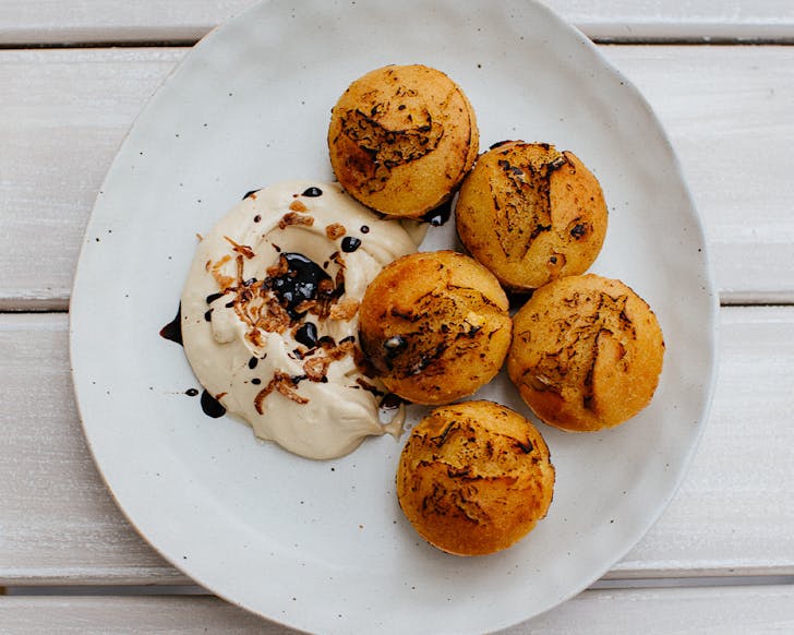 Five cornbread spheres with whipped brown butter dipping sauce on a white plate. 